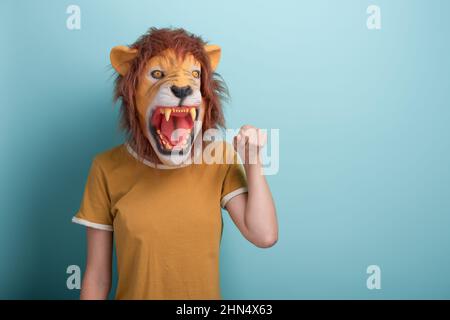 Jeune femme dans le masque de lion tient la main levée pour le poing bosse, isolé sur fond bleu avec l'espace de copie. Banque D'Images