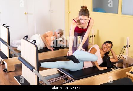 Femme hispanique faisant de l'exercice sur les pilates réformateur avec une jeune femme entraîneur Banque D'Images