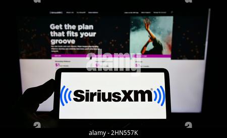 Personne détenant un téléphone intelligent avec le logo de la société de radiodiffusion américaine Sirius XM Holdings Inc. À l'écran devant le site Web. Mise au point sur l'affichage du téléphone. Banque D'Images