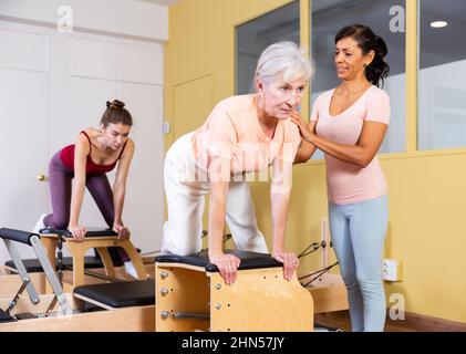 Femme sénior pratiquant le pilates sur une chaise combinée avec une formatrice hispanique féminine Banque D'Images