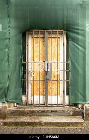 Porte fermée à clé dans un ancien bâtiment en cours de rénovation enveloppée dans des filets de sécurité de construction. Banque D'Images