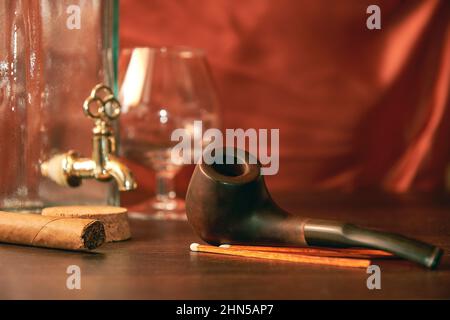 Pipe à fumer avec verre de brandy vide et bouteille et tabac sur la table en bois. Collection vintage pour la détente de l'homme Banque D'Images