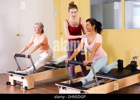 Femme hispanique faisant de l'exercice sur les pilates réformateur avec une jeune femme entraîneur Banque D'Images
