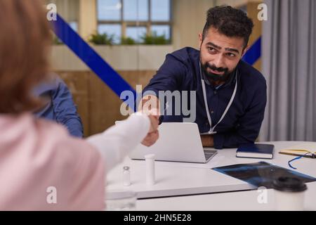 Jeune expert médical sérieux en tenue formelle saluant la femme clinicien ou l'assistance par poignée de main après être venu aux termes lors de la réunion Banque D'Images