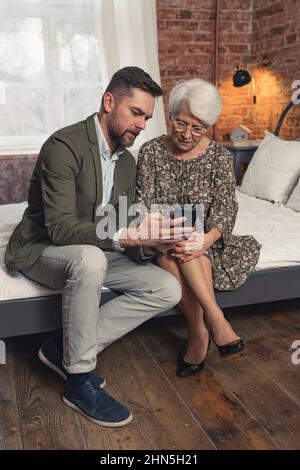 homme du millénaire barbu expliquant à sa mère âgée comment les smartphones fonctionnent vertical. Photo de haute qualité Banque D'Images