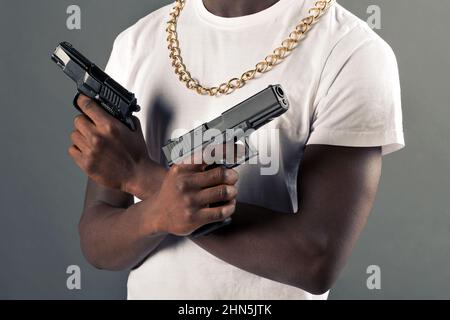 Récolte dangereuse anonyme Africain américain en chaîne avec des armes noires dans les mains debout sur fond gris en studio léger Banque D'Images