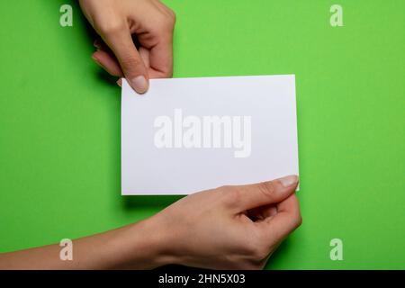 deux mains de sexe féminin tenant un morceau de papier vierge avec un espace de copie devant un carton de fond vert Banque D'Images