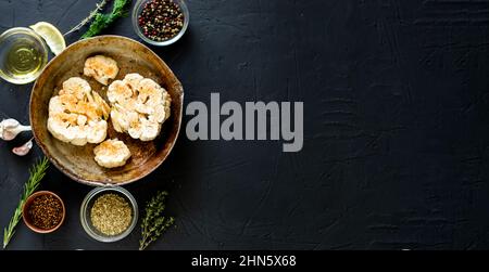 Cuisson du steak de chou-fleur. Le chou-fleur cru parsemé d'épices se trouve dans une poêle à frire. Huile d'olive, herbes, diverses épices à proximité. Arrière-plan sombre. Copie Banque D'Images