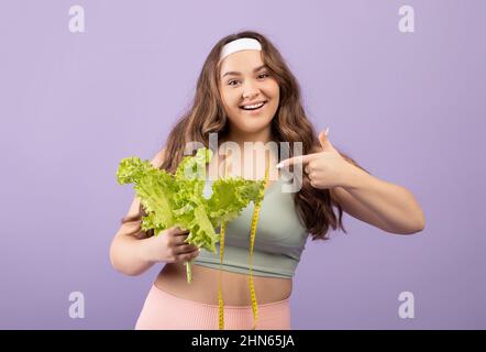 Portrait d'une jeune femme européenne plus heureuse en vêtements de sport avec mètre ruban à bout de doigt sur la salade Banque D'Images