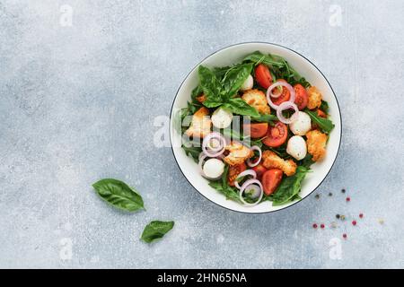 Panzanella, salade de pain italienne. Cuisine traditionnelle italienne avec tomates, boules de mozzarella, basilic, oignon et pain sur fond gris clair. Tradition Banque D'Images