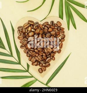 Composition écologique avec grains de café naturels sur papier artisanal en forme de coeur avec feuilles de palmier sur fond artisanal. Concept de naturel, Banque D'Images