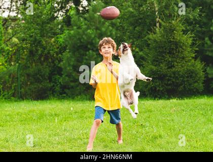 Bonne formation d'enfant pour jouer au football américain sur la pelouse de la cour. Balle de capture pour enfant et chien. Banque D'Images