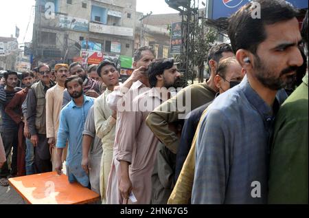 Les gens se sont rassemblés dans une file d'attente pour acheter des sacs de farine sur le prix des subventions d'un magasin de services publics mobiles vendu par le gouvernement de Sindh, comme le prix des articles généraux utilisés quotidiennement ont touché le ciel en raison de la hausse des prix dans le pays, sur une route à Hyderabad le lundi 14 février, 2022. Banque D'Images