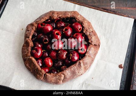 Galette de cerise au chocolat non cuite fraîchement préparée : tarte aux fruits crus sur une poêle en papier parchemin bordée de feuilles Banque D'Images