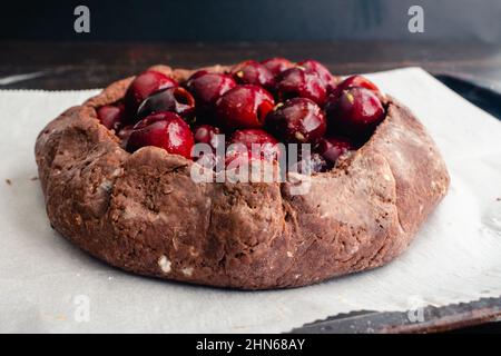 Galette de cerise au chocolat non cuite fraîchement préparée : tarte aux fruits crus sur une poêle en papier parchemin bordée de feuilles Banque D'Images