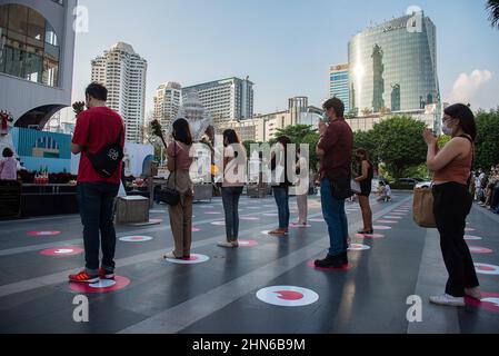 On voit des gens prier au sanctuaire Trimuriti de Bangkok. L'événement « priez et balayez vers la droite » organisé par l'application de rencontres en ligne Tinder, avec des marqueurs de logo social Distancing Tinder sur le terrain de prière, une cabine photo où les gens peuvent prendre des photos de profil pour leurs nouveaux comptes, et des ensembles gratuits, au sanctuaire Trimuriti le jour de la Saint-Valentin à Bangkok, en Thaïlande. Le Trimuriti l'un des dieux hindous est connu pour être le dieu de l'amour. Les gens viennent adorer au sanctuaire de Trimurti avec des offrandes de roses rouges dans l'espoir qu'ils rencontreront leur soulmate. Banque D'Images