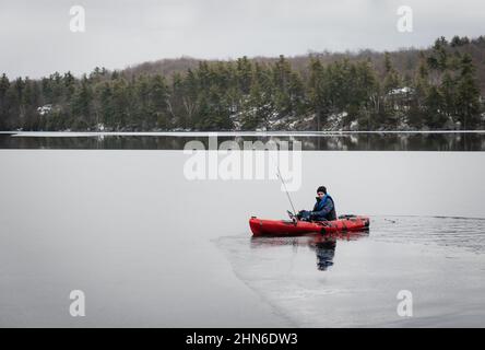 Jeune garçon assis dans un kayak de pêche sur un lac glacé en hiver. Banque D'Images