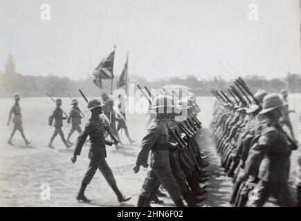 Un tableau historique des fantassins de l'armée britannique marchant dans deux rangs avec des fusils court à épaulement de Magazine Lee Enfield et des baïonnettes fixes, escortant les couleurs régimentaires et les couleurs des rois sur un terrain de parade. On croyait être en Inde britannique c. début du 20th siècle . Banque D'Images