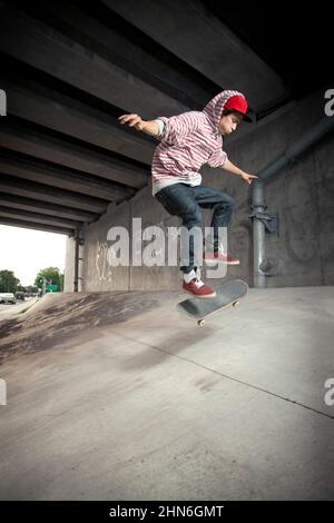 Skateboarder faisant un kickflip sous le passage Banque D'Images