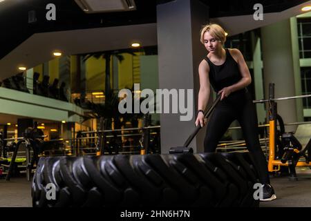 Roue avec sledgehammer girl stands pneu de forme physique musculaire, dans l'après-midi l'entraînement de l'équipement de bodybuilder santé de traîneau, l'urning muscle. Tresses Banque D'Images