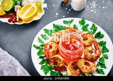 Crevettes grillées sur une assiette blanche avec persil frais, épices et citron, crevettes frites avec sauce dans un pot Banque D'Images