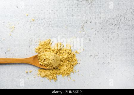 Poudre de moutarde dans une cuillère en bois sur fond blanc. Banque D'Images