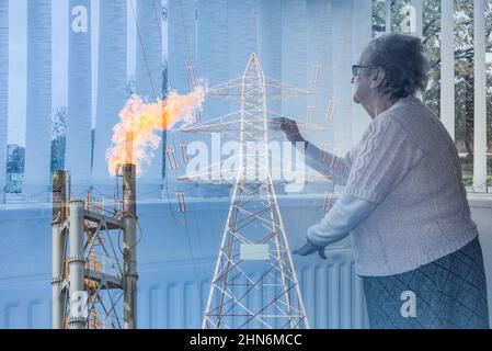 femme de 90 ans regardant par la fenêtre avec la main sur le radiateur. Pylône d'électricité et feu de gaz industriel image de cheminée mélangée. Concept de crise d'énergie. Banque D'Images