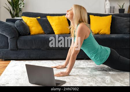 Femme âgée en position de planche regardant le tutoriel vidéo de sport sur l'ordinateur portable. Une femme d'âge moyen mène un mode de vie actif, s'exerçant à la maison, apprenant le yoga en ligne Banque D'Images
