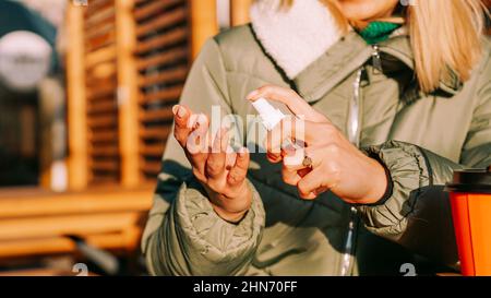 Une jeune femme dans une veste chaude traite ses mains avec un antiseptique à l'extérieur. Gros plan Banque D'Images