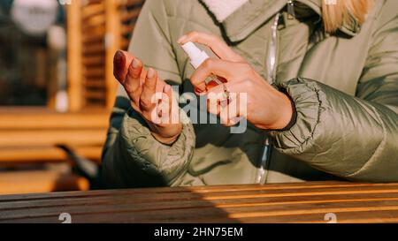 Une jeune femme dans une veste chaude traite ses mains avec un antiseptique à l'extérieur. Gros plan Banque D'Images