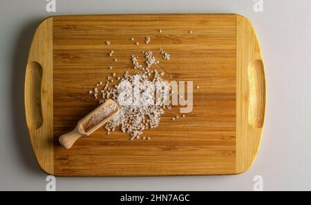 Salez dans une cuillère en bois sur une planche de cuisine en bois. Grandes pièces de sel de mer dans une petite cuillère en bois. Banque D'Images