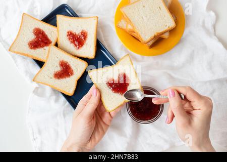 La fille fait un toast sur lequel le coeur est fait de confiture. Petit déjeuner surprise au lit. Romance pour la Saint-Valentin Banque D'Images