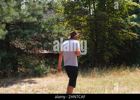 Homme en chapeau. Portrait d'un fermier souriant avec de l'herbe verte et de la nature des arbres en arrière-plan. Jeune homme portant un chapeau de cow-boy sur le terrain. Gros plan. Personne heureuse Banque D'Images