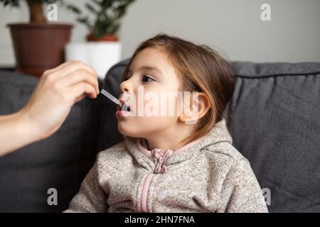 Portrait d'une jeune fille d'âge préscolaire de race blanche prenant des vitamines avec des gouttes à la maison. Concept d'immunité Banque D'Images