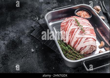 Cuisson du pain de viande cru avec de la viande de bœuf hachée et du bacon dans un plateau en acier, pain de viande frais. Arrière-plan noir. Vue de dessus. Copier l'espace Banque D'Images