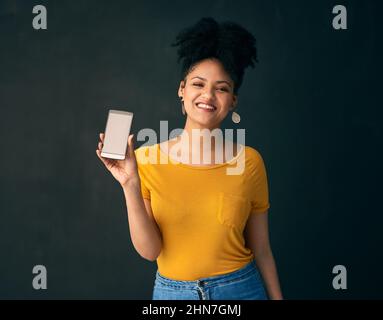 Découvrez cette incroyable application mobile. Photo d'une jeune femme tenant un téléphone portable tout en posant sur un fond gris. Banque D'Images