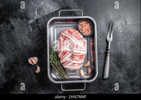 Cuisson du pain de viande cru avec de la viande de bœuf hachée et du bacon dans un plateau en acier, pain de viande frais. Arrière-plan noir. Vue de dessus Banque D'Images