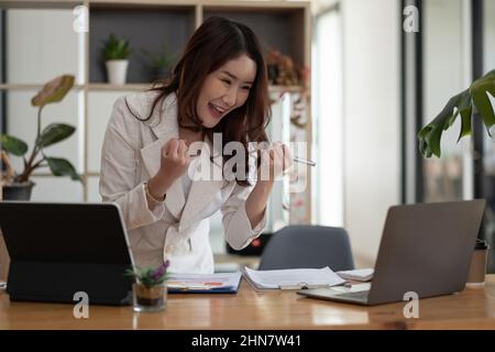 Entrepreneur de belle entreprise asiatique jeune femme travaillant avec un ordinateur portable et célébrant à la maison avec son succès de travail gai et bonheur, petit Banque D'Images