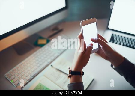Textes importants pour le patron. Prise de vue rognée d'une femme méconnaissable à l'aide d'un téléphone portable au bureau. Banque D'Images