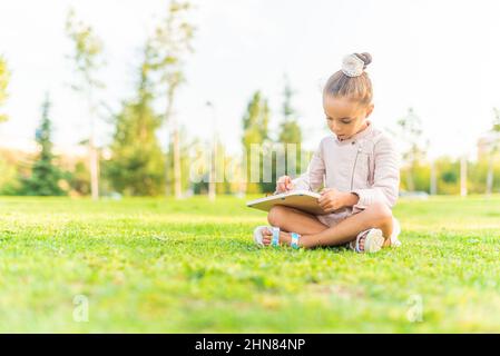 fille assise dans un parc jouant avec un tableau à dessin. Banque D'Images