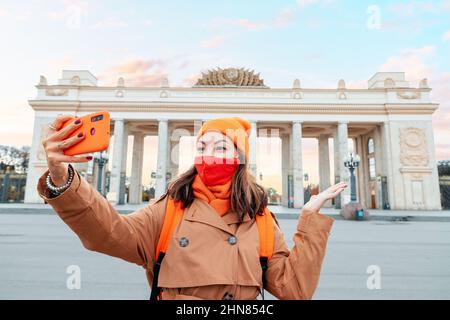 Une femme dans un masque médical de protection pose et prend un selfie sur le fond du parc Gorky à Moscou. Voyages et voyages d'affaires Banque D'Images