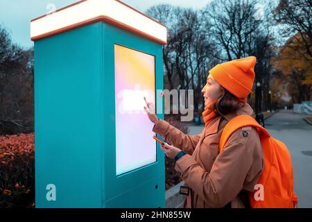 Une femme utilise un kiosque en libre-service pour imprimer des photos depuis son smartphone dans une rue urbaine Banque D'Images