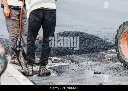 Travaux manuels lourds et sales sur la pose d'asphalte frais et de bitume sur une rue urbaine Banque D'Images