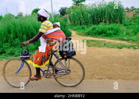 Une femme burkinabée portant son bébé sur le dos tout en montant son vélo dans le centre du Burkina Faso . Banque D'Images