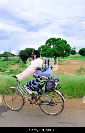 Une femme burkinabée portant son bébé sur le dos tout en montant son vélo dans le centre du Burkina Faos. Banque D'Images