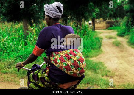 Une femme burkinabée portant son bébé sur le dos tout en montant son vélo dans le centre du Burkina Faos. Banque D'Images