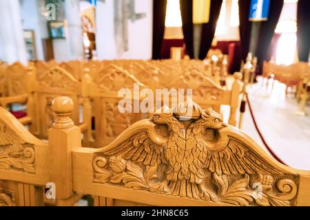 Aigle à deux têtes sculpté sur un banc en bois à l'intérieur de la majestueuse église Saint-Demetrios. Concept de pèlerinage et de culte Banque D'Images