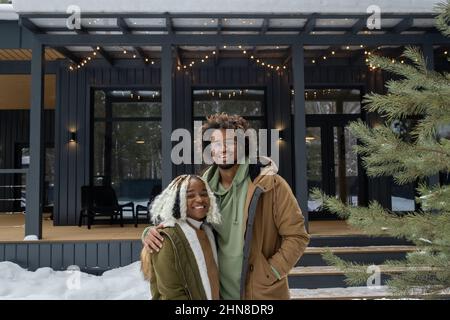 Portrait d'un jeune couple africain embrassant et souriant à l'appareil photo tout en se tenant à l'extérieur près de leur maison de campagne Banque D'Images