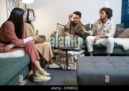 Un groupe d'amis se réunissant à la maison le week-end et s'amusant à jouer, ils s'assoyent sur un canapé et boivent de la bière Banque D'Images