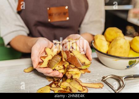 Pelures de pommes de terre dans les mains de la cuisinière femelle. Utilisation et transformation des déchets alimentaires, compostage, afin d'enrichir la fertilité des sols. Tri des ordures à la maison Banque D'Images